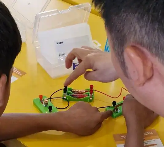 Youths participating in a hands-on engineering session with DLE volunteers, exploring electrical connections and competing in a solar grasshopper challenge.